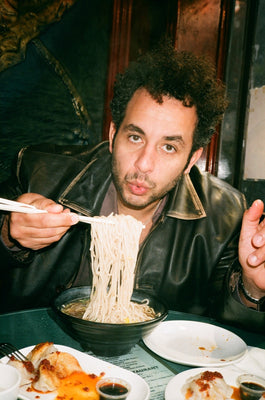 Kareem Rahma eating a bowl of noodles in a leather jacket