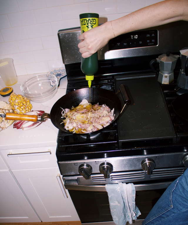 Person squeezing olive oil into wok filled with shallots